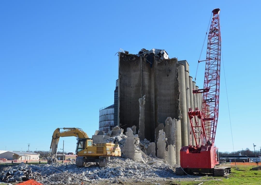 Concrete silos being demolished on a construction site, generating large dust clouds that require certified monitoring